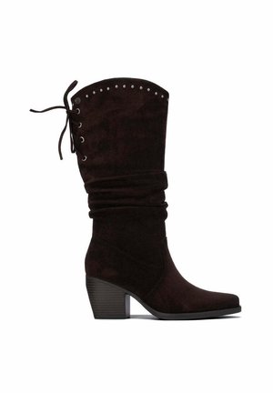 Bota alta de ante marrón oscuro con tacón bloque bajo, tachuelas decorativas cerca de la parte superior, caña holgada y detalle de cordones en el lateral.