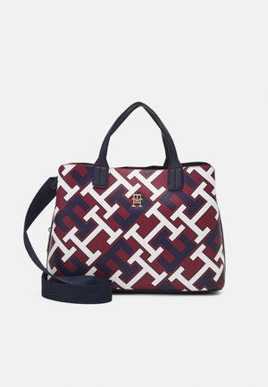 Kleine handtas met bordeaux, marineblauw en wit geometrisch patroon, marineblauwe handgrepen, verstelbare schouderriem en gouden merklogo aan de voorkant.