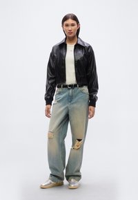 Μαύρο κοντό μπουφάν, λευκό πουλόβερ, ανοιχτό μπλε ξεβαμμένο παντελόνι με φαρδιές παντελόνες και σκισίματα· μεταλλικά ασημί αθλητικά παπούτσια· απλή μαύρη ζώνη.