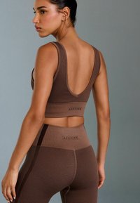 Brown ribbed activewear set featuring a low-back sports bra and high-waisted leggings, with textured patterns and subtle logo detailing.