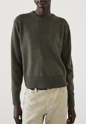 Dark green long-sleeve sweater worn over light beige pants with a black belt, shown on a person from shoulders to hips.