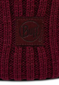 Burgundy knit beanie with ribbed texture, featuring a rectangular brown leather patch embossed with "Buff" logo.