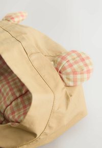 Bézs sapka rózsaszín és krémszínű kockás díszítéssel, kerek fülekkel és puha, texturált belső résszel. Varrt kialakítás, sima felülettel.