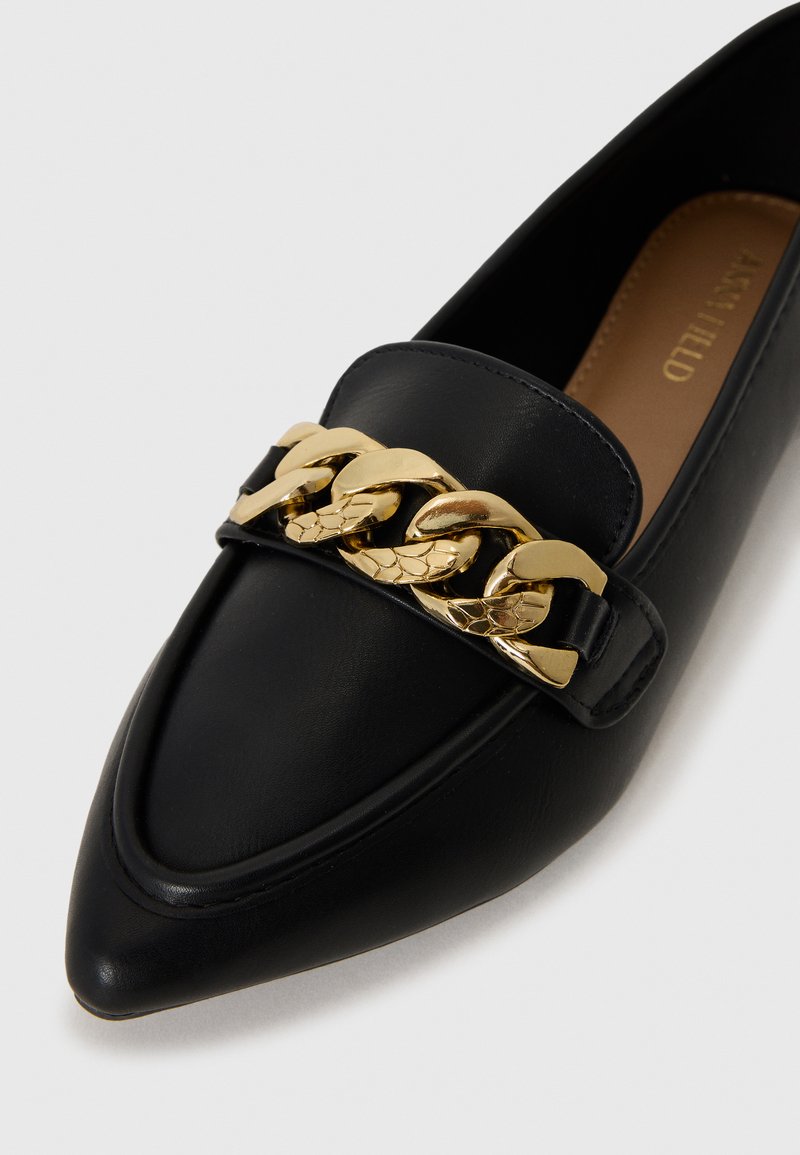 Mocassini neri in pelle con punta, caratterizzati da un accento di catena dorata sulla parte anteriore. Texture liscia con dettagli di cucitura lungo i bordi.