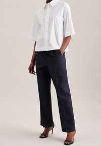 Vit kortärmad skjorta med knappar, matchad med mörkblå vida byxor och svarta klacksandaler. Slät tyg; avslappnad passform.