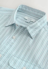 Jasnoniebieska koszula na guziki z cienkimi pionowymi paskami w kolorach morskim i różowym. Posiada kołnierz typu klasycznego i pojedynczą kieszeń na piersi. Wykonana z bawełny.