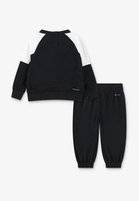 Sweatshirt noir avec des accents blancs et des poignets élastiques, associé à un pantalon de jogging noir assorti avec une taille élastique.