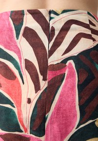 Blumendruckstoff mit großen Blättern in rosa, grün und braunen Farbtönen. Reißverschlussverschluss hinten mit passender Nahtdetail.