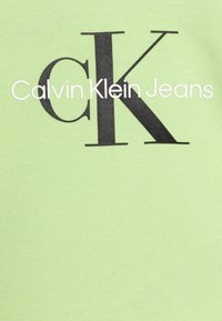 Jasnozielony bawełniany T-shirt z wyrazistym czarnym logo "CK" oraz napisem "Calvin Klein Jeans" poniżej, o gładkiej fakturze i standardowym kroju.