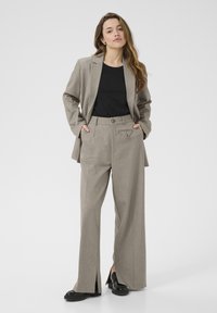 Lys grå skræddersyet blazer med matchende brede bukser, der har en subtil tekstur og en trekantet lomme-detale. Sort top og sko.
