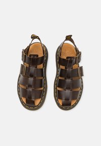 Tummanruskeat nahkasandaalit, joissa on kudottu muotoilu, kaksi solkiyksityiskohtaa, teksturoitu pohja ja keltainen ommel reunoilla.