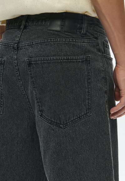 Fekete farmernadrág függőleges bordázott mintázattal, két hátsó zsebbel és bőrpánttal ellátott derékrésszel. Slim fit fazon.