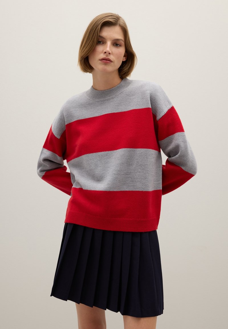 Maglione a righe rosse e grigie in maglia con scollo tondo e maniche lunghe, abbinato a una gonna plissettata blu navy. Tessuto morbido, design casual.