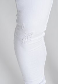 Jeans de mezclilla blanca con un diseño ajustado y parches desgastados en la rodilla, y una textura suave.