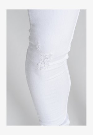 Jean en denim blanc avec une coupe ajustée, présentant des zones de déchirure au niveau des genoux et une texture lisse.