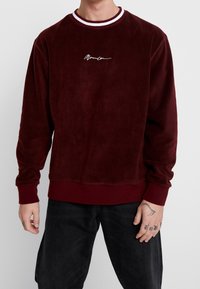 Bordeaux fleece sweatshirt med ribbet rød og hvid crew neck, brede manchetter, en afslappet pasform og hvid kursiv logo broderi.