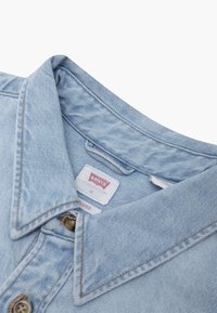 Light blue denim shirt with a classic collar, two buttons at the neck, and a woven label reading "Levi's M Relaxed" on the inner side.