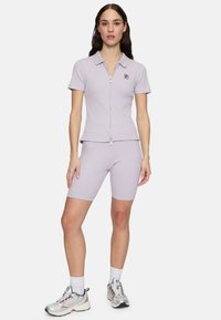 Lichtpaarse geribbelde zip-up polo en bijpassende shorts, met een klein logo op de borst, gecombineerd met zilveren sport sneakers.