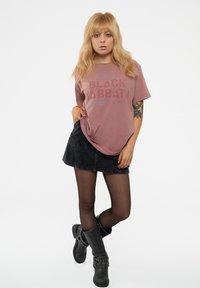 Short-sleeve, faded mauve t-shirt with "BLACK SABBATH" print; paired with a black denim skirt and black heeled boots. Smooth fabric texture.