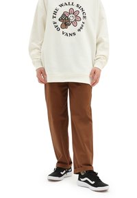 Kremowa bluza z graficznym logo i brązowe spodnie; stylizowana z czarno-białymi sneakerami, o gładkiej fakturze i luźnym kroju.