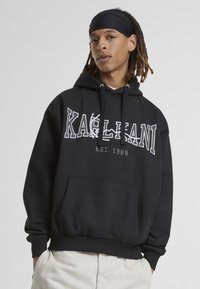 Felpa nera realizzata in morbido tessuto, con tasca frontale e audace grafica bianca "KALAHNI EST. 1989".