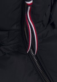 Zwarte gewatteerde jas rits met een gestructureerde oppervlakte, voorzien van een kleurrijke gestreepte trekker in rood, wit en blauw.