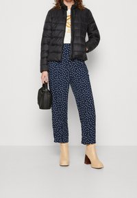Giacca a vento nera, t-shirt bianca con grafiche, pantaloni navy a pois, stivaletti beige con tacco, e una piccola borsa nera.