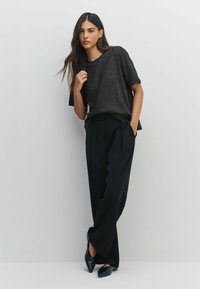 Schwarzes kurzes T-Shirt mit strukturierter Oberfläche, kombiniert mit hochgeschnittenen schwarzen weiten Hosen und spitzen schwarzen Schuhen.