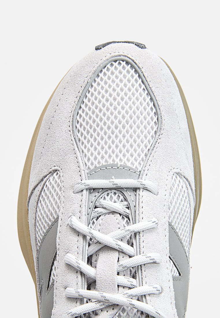 Baskets de sport gris clair avec une tige en maille et des accents en daim. Présente des lacets plats et une semelle en caoutchouc neutre.