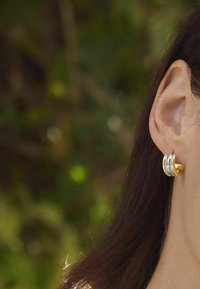 Orecchini a cerchio in oro e argento con un design a strati, con una finitura liscia e una leggera curvatura, indossati sull'orecchio di una persona.