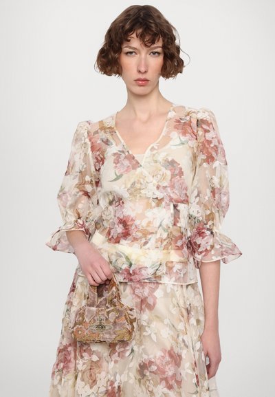 Doorzichtige bloemenblouse met pofmouwen in zachte pasteltinten, gecombineerd met een kleine, versierde fluwelen handtas met metalen accenten.