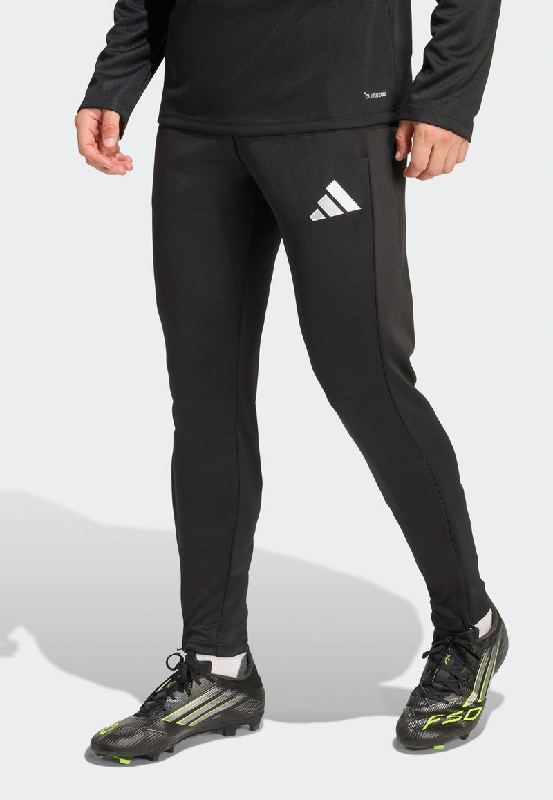 Sorte atletikbukser med en tætsiddende pasform, der har et hvidt Adidas-logo, glat tekstur og er skåret til bevægelsesfrihed. Kombineret med sorte fodboldstøvler.