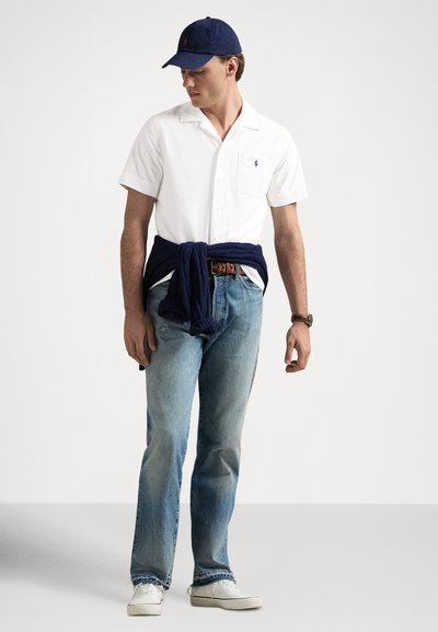 Balta īsroku krekls, zilas džinsa bikses, tumši zila džemperis sasiets ap vidukli, baltas sporta kurpes un tumši zila cepure. Ikdienas, brīva piegriezuma ar kabatas detaļu.