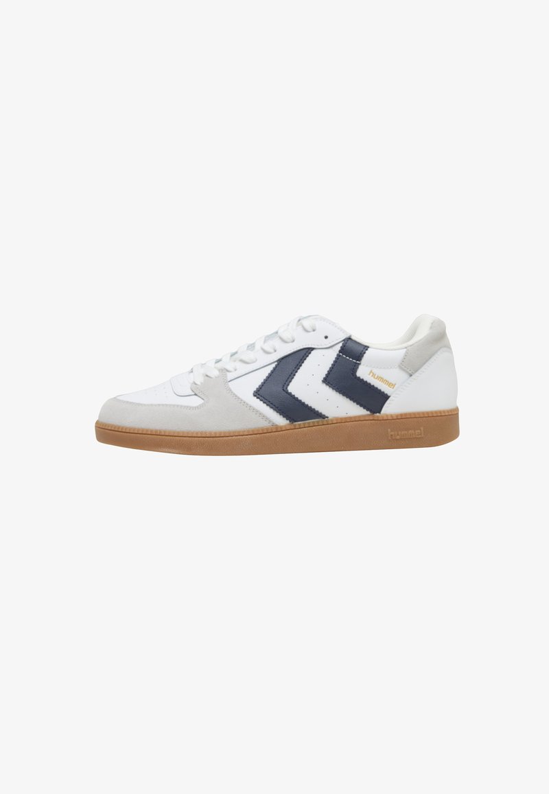 Baskets blanches avec bout en daim gris, bandes en chevron bleu marine, semelle gomme, et lacets blancs, marquées "hummel" sur le côté et la semelle.