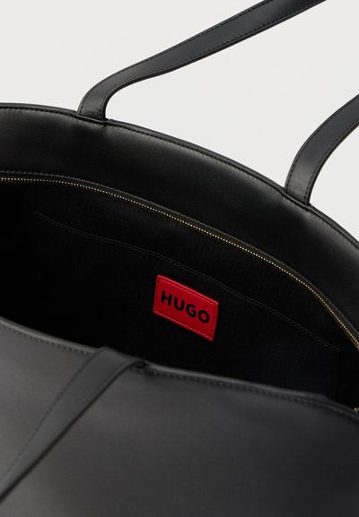 Sac cabas en cuir noir avec double poignée, montrant une poche intérieure zippée et une étiquette de marque "HUGO" rouge à l'intérieur.