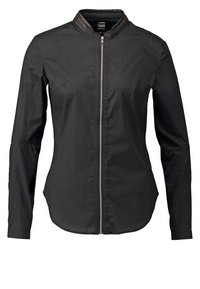 Veste noire à manches longues avec fermeture éclair devant et col montant, présentant une silhouette légèrement ajustée.