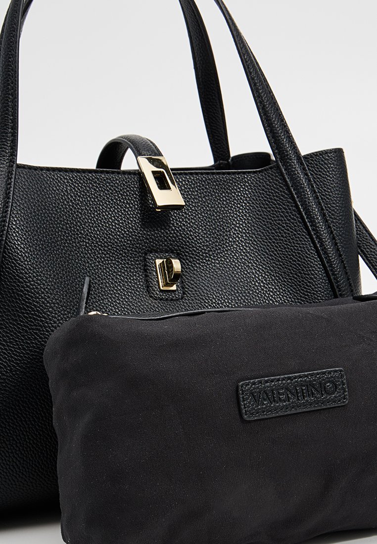 Schwarze, strukturierte Lederhandtasche mit einer goldfarbenen Schnalle. Verfügt über einen abnehmbaren schwarzen Stoffbeutel mit einem Logotag.