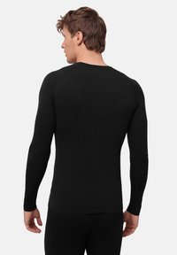 Musta pitkähihaisen paita, jossa pyöreä pääntie, istuva malli ja saumaton olkapää, valmistettu sileästä, joustavasta kankaasta.