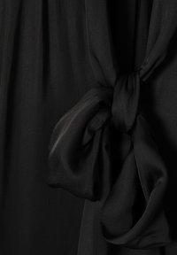 Black, sheer fabric with a soft texture, featuring a knotted accent. The fabric drapes elegantly, creating a flowing silhouette.
