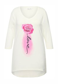 Maglietta a maniche lunghe color crema con scollo a V, caratterizzata da una grafica di una rosa rosa e la parola "love" in corsivo nero sotto di essa. Tessuto morbido.