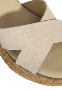 Sandal en suède beige à brides croisées avec une semelle en liège texturé et une doublure intérieure lisse, présentant un bout arrondi et un talon plat.