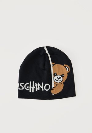 Gorro de punto negro tipo beanie con un osito de peluche marrón asomándose desde detrás de una línea vertical blanca y mostrando parcialmente la palabra "MOSCHINO".