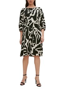 Robe à motifs noir et blanc avec des manches bouffantes, un col rond et une silhouette évasée. Associée à des talons noirs à lanières.