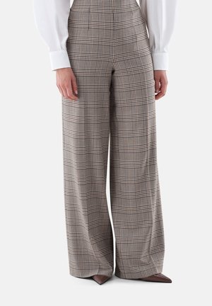Person trägt karierte, hoch taillierte, weit geschnittene Hose mit braunen spitzen Schuhen und ein weißes Langarmhemd mit geknöpften Manschetten.