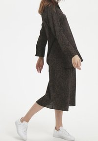 Brun leopardprickig blus med avslappnad passform, matchad med en midi kjol. Bärs med vita sneakers, vilket visar en avslappnad stil.