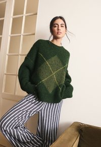 Green knitted sweater with diamond pattern in shades of green and yellow, paired with blue and white striped wide-leg pants.