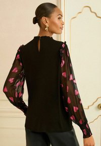 Fekete felső áttetsző puffos ujjakban, rózsaszín szívmintával. Ráncolt nyakrésszel és kulcslyuk részlettel a háton. Sima anyagú test.