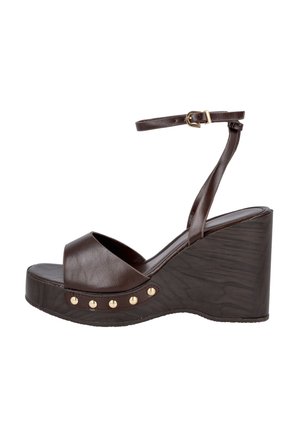 Sandalia de cuña de piel marrón con punta abierta, tira en el tobillo con hebilla dorada y detalles de tachuelas doradas a lo largo del borde de la suela.