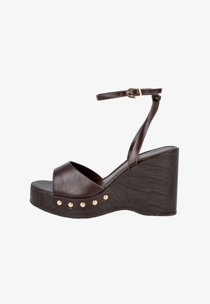 Sandalia de cuña de piel marrón con punta abierta, tira en el tobillo con hebilla dorada y detalles de tachuelas doradas a lo largo del borde de la suela.