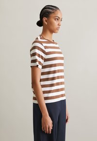 Striped t-shirt featuring horizontal brown and white stripes, short sleeves, round neckline, and a relaxed fit. Paired with navy pants.